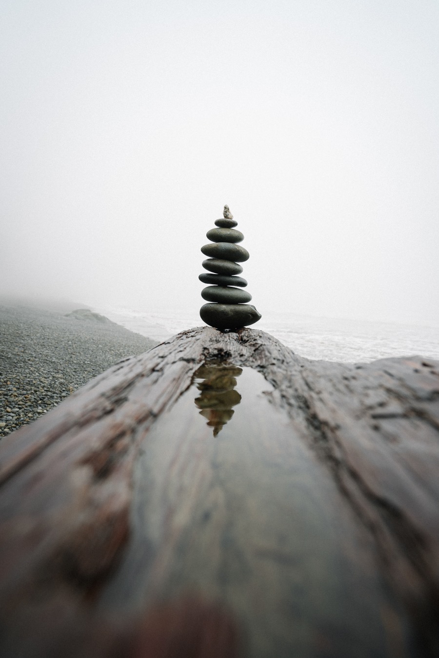 This is an image of a set of stones balanced on the end of a log by the beach