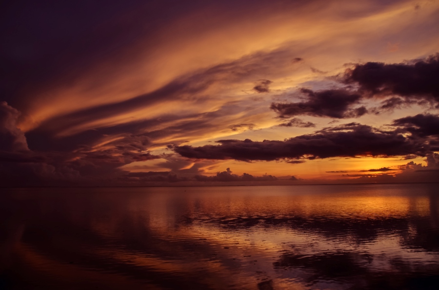 This is a picture of the ocean with the sunset in the background and clouds covering some of the sunset