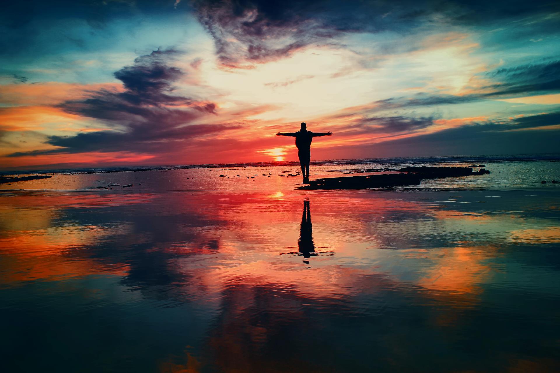 This is an image of a man standing on the edge of the ocean looking out to the sunset